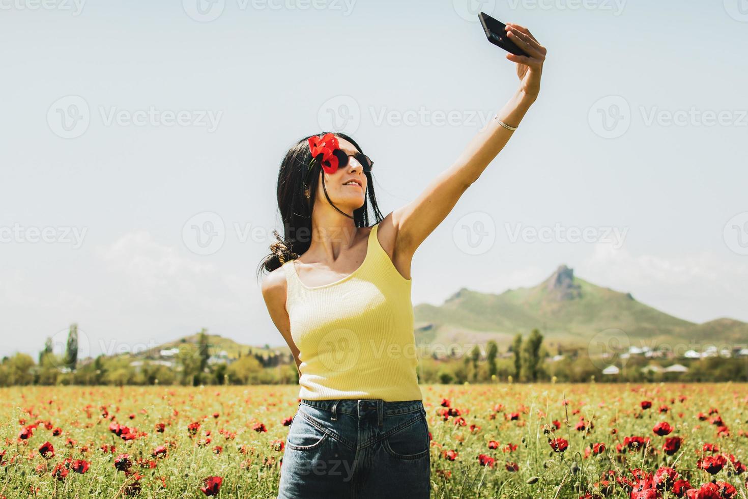 caucasico giovane spensierato donna hold papavero fiore nel orecchie In piedi nel papavero fiore campo prendere autoscatto godere primavera. concetto la libertà e estate gioia nel natura foto