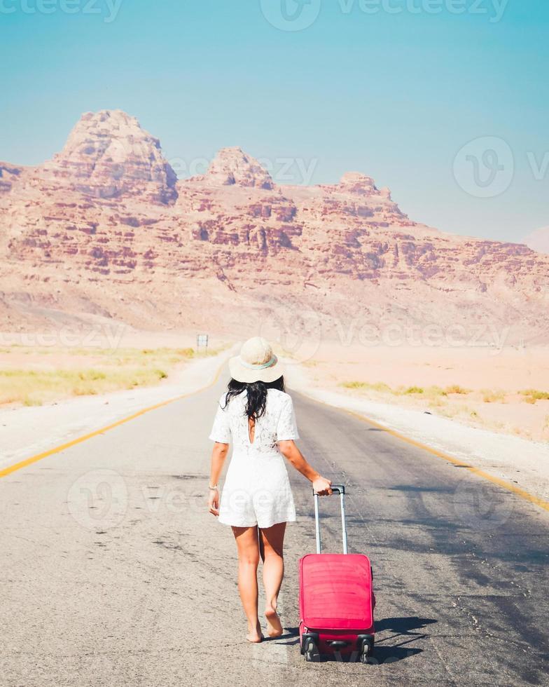 cinematico viaggio sfondo giovane spensierato caucasico viaggiatore turista su strada camminare trascinare bagaglio a piedi nudi per bellissimo paesaggio. viaggio concetto direzione e Il prossimo viaggio destinazione foto