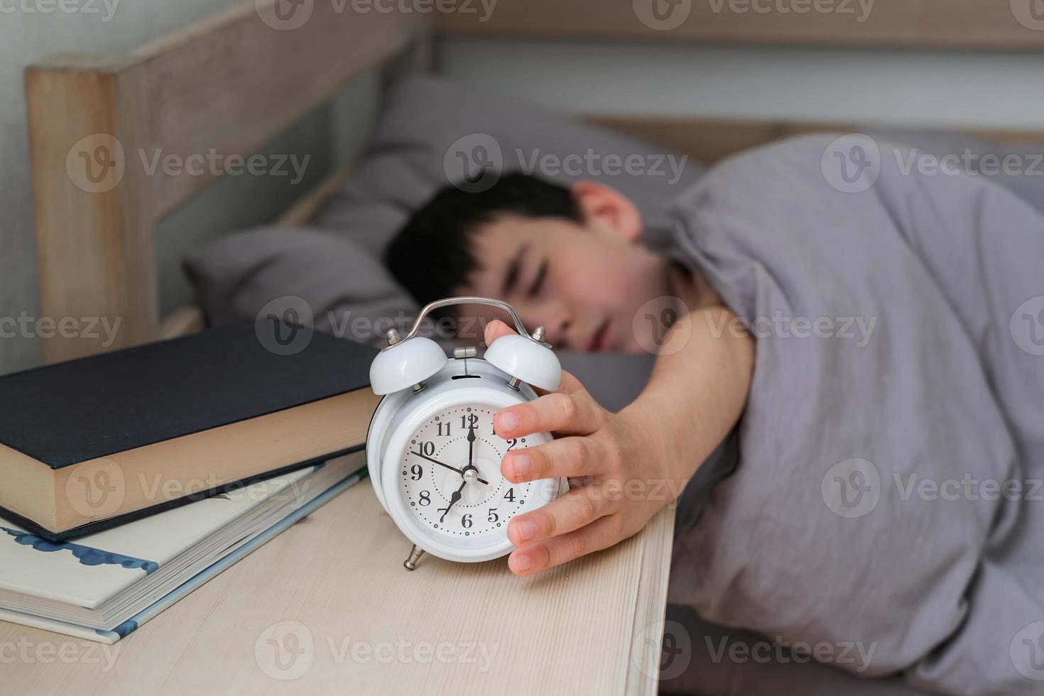 assonnato ragazzo raggiunge per il allarme orologio. mattina di il scolaro foto