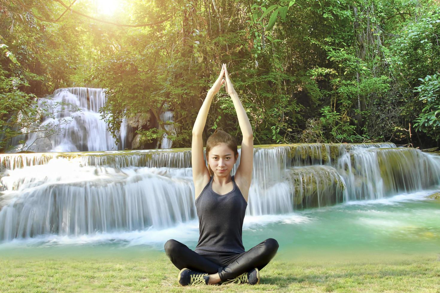 donna asiatica atletica in posa yoga con sfondo cascata foto