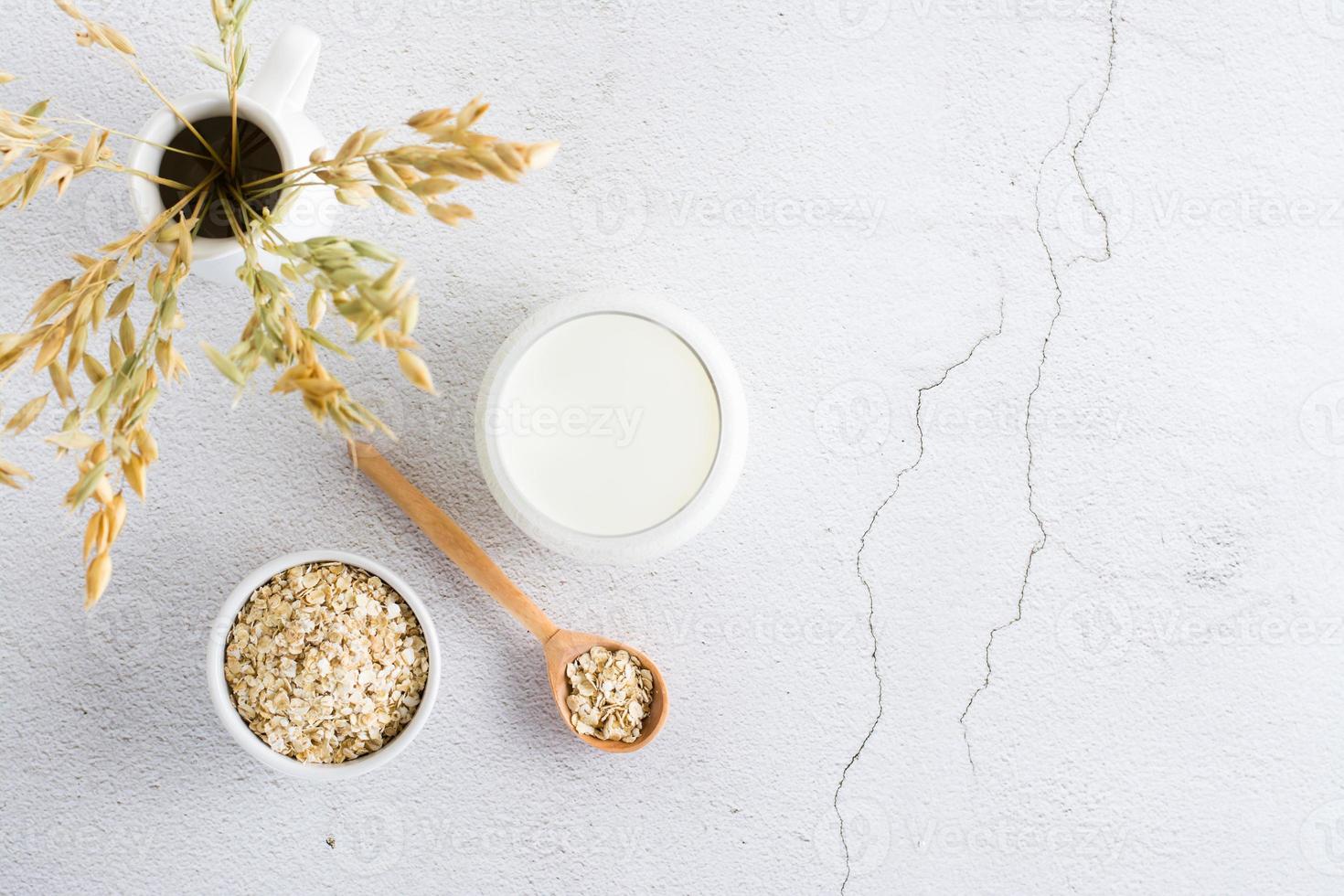 avena latte nel un' bicchiere, fiocchi d'avena nel un' ciotola e orecchie nel un' brocca su un' leggero tavolo. alternativa pianta cibo. superiore Visualizza. copia spazio foto