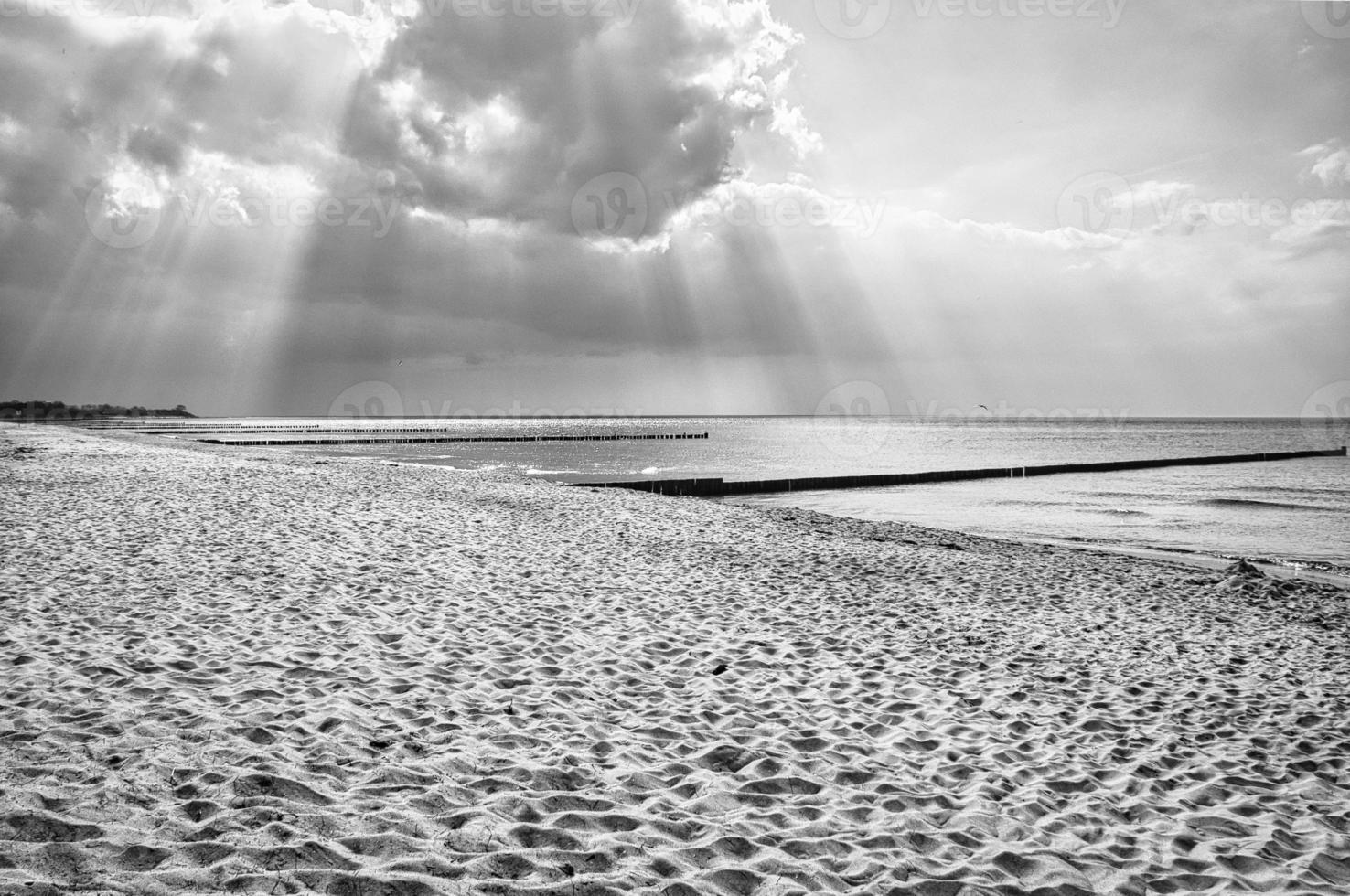 sole raggi splendente attraverso denso nuvole su il spiaggia di il baltico mare. nero e bianca foto