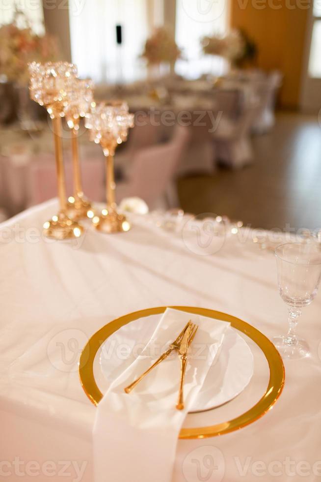 tavolo decorazione con rosa tovaglia, cristallo candelieri con candele e bianca rosa fiori nel ristorante . elegante nozze giorno. ambientazione tavolo con oro piatto, forchetta e coltello foto