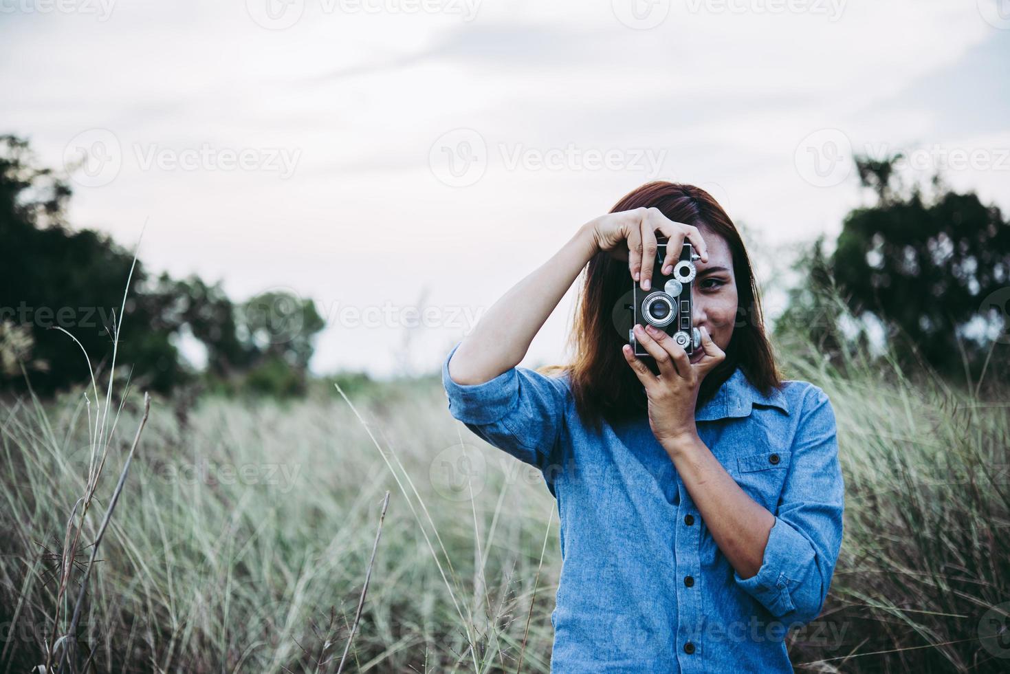 felice giovane donna hipster con fotocamera vintage in campo foto