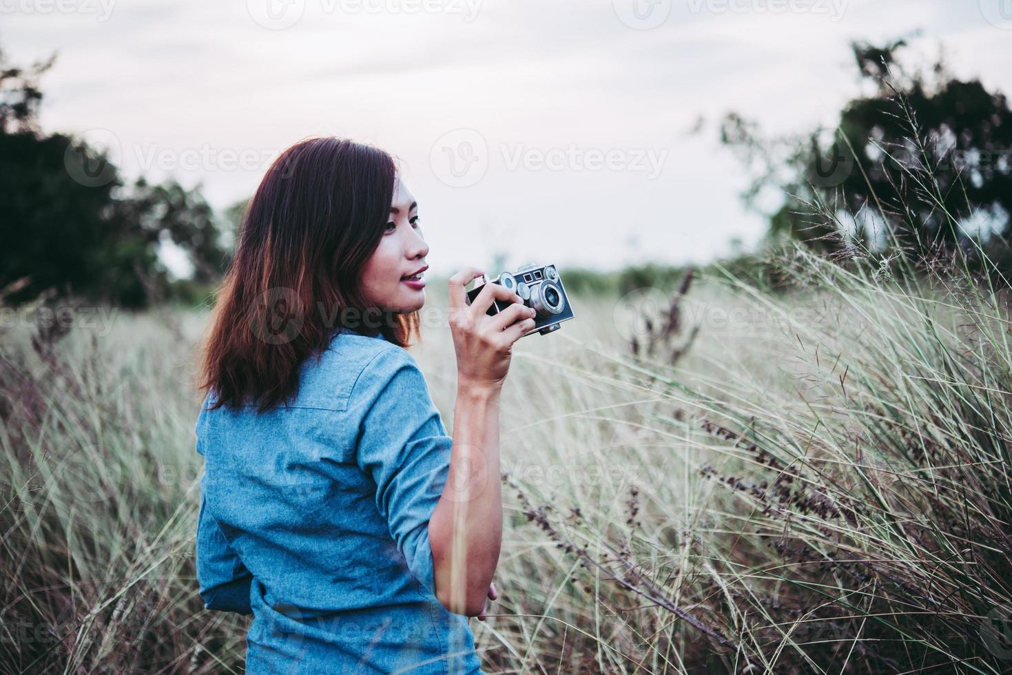 felice giovane donna hipster con fotocamera vintage in campo foto