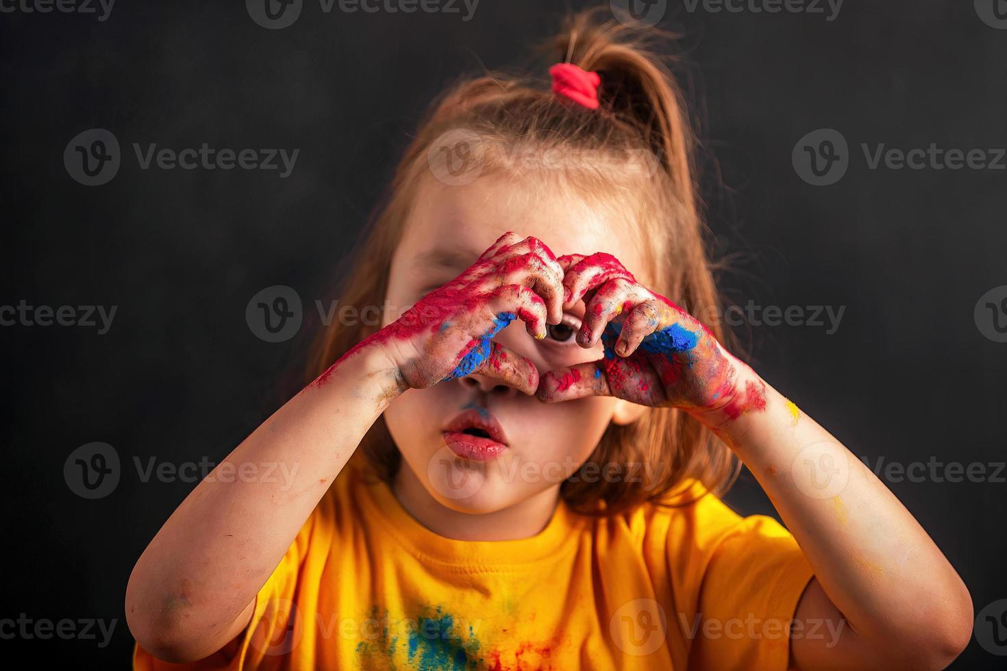 avvicinamento poco ragazza piegato sua dita nel il forma di un' cuore, sua mani nel multicolore holi colori, un' cartello di amore. indiano Festival di colori holi foto