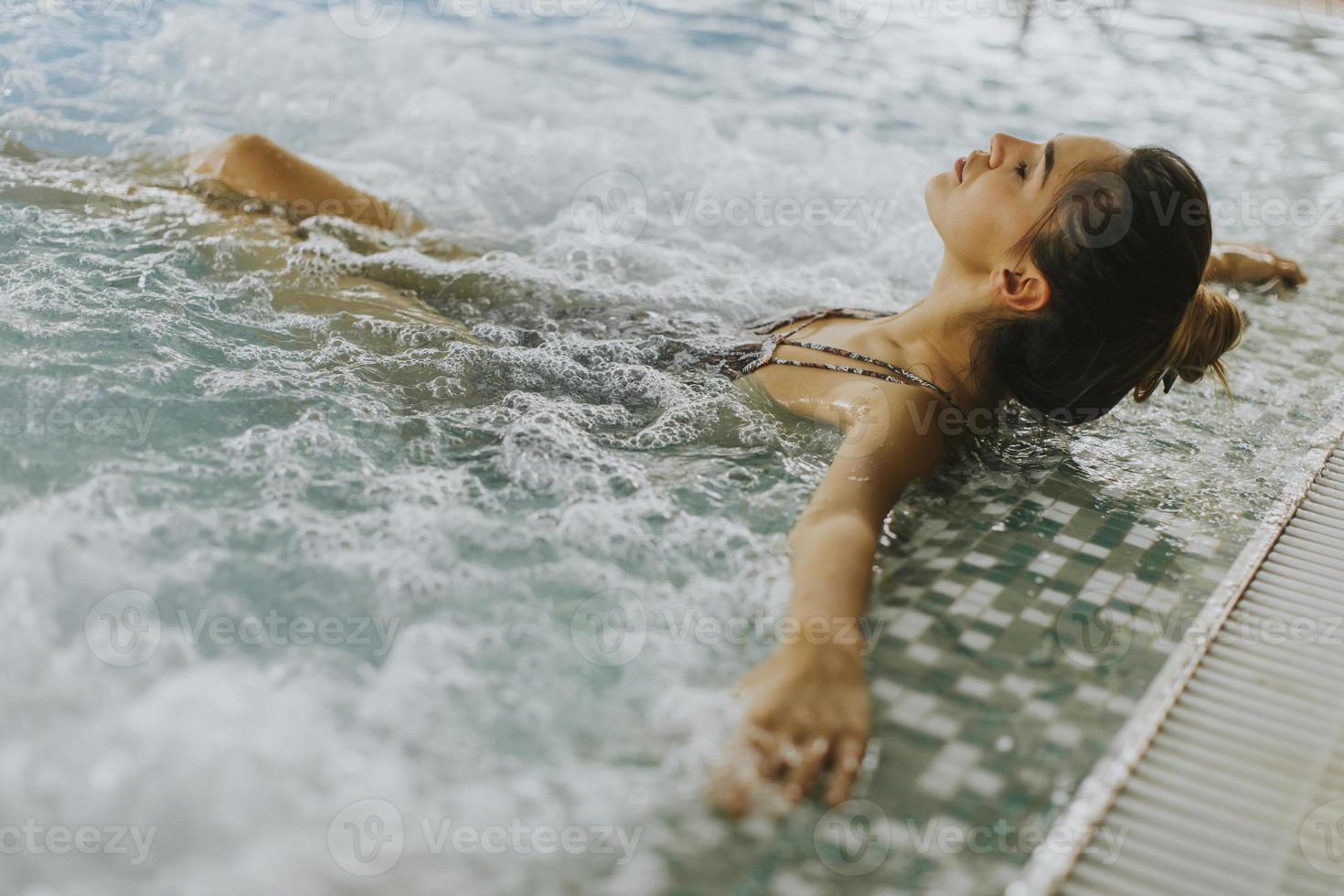 giovane donna che si distende nella vasca idromassaggio a bordo piscina foto