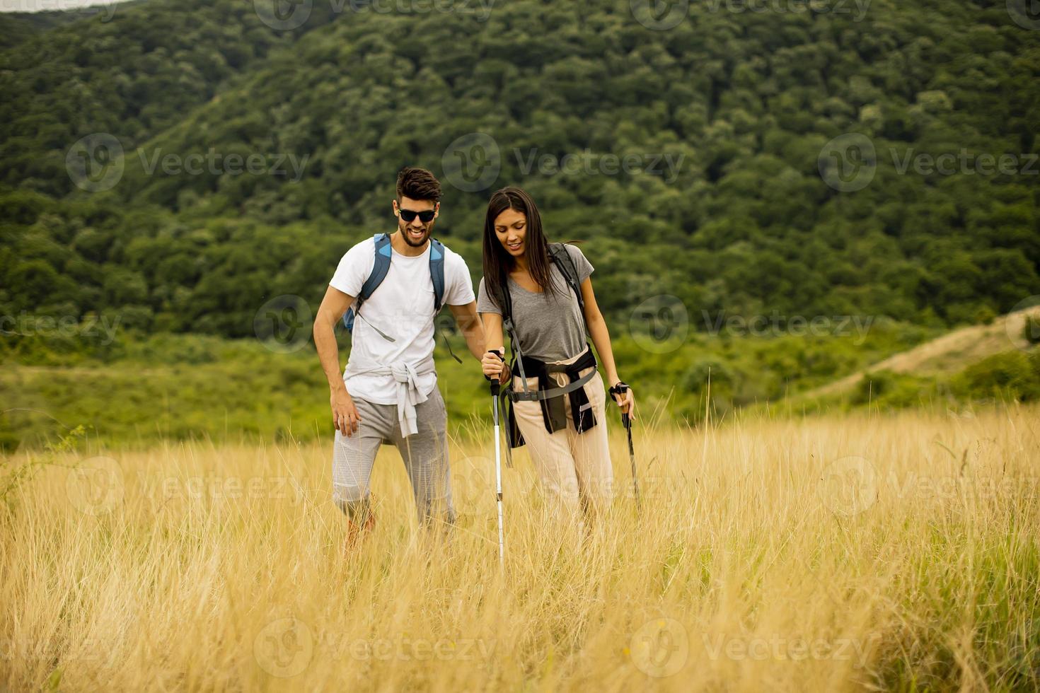 coppia sorridente che cammina con zaini su verdi colline foto