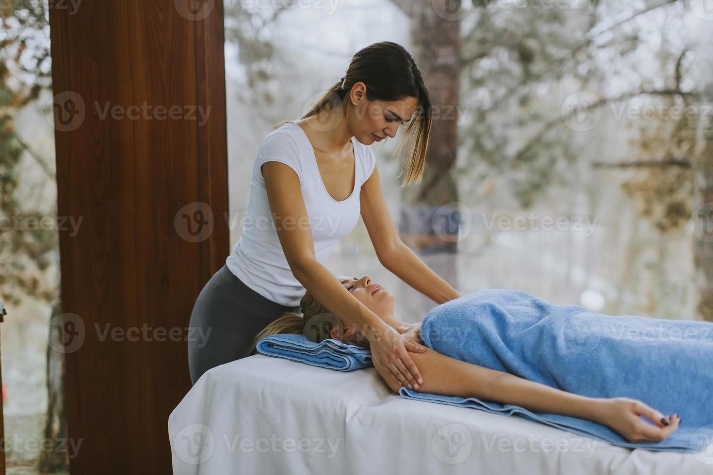 bella giovane donna sdraiata e con massaggio alla spalla nel salone spa durante la stagione invernale foto