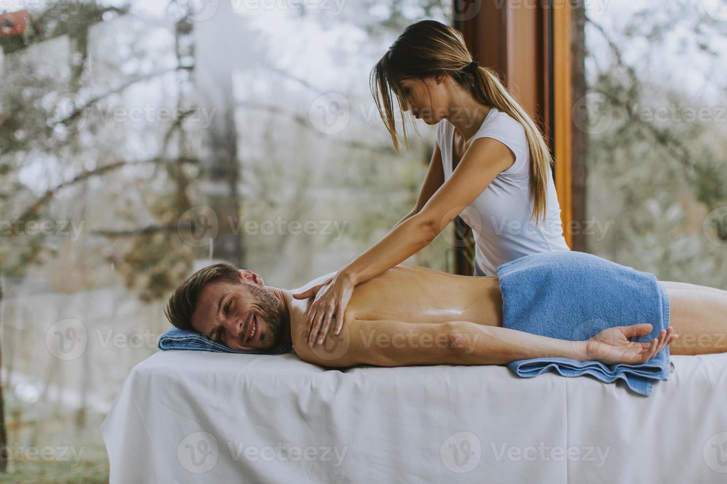 bel giovane uomo sdraiato e con massaggio alla spalla nel salone spa durante la stagione invernale foto