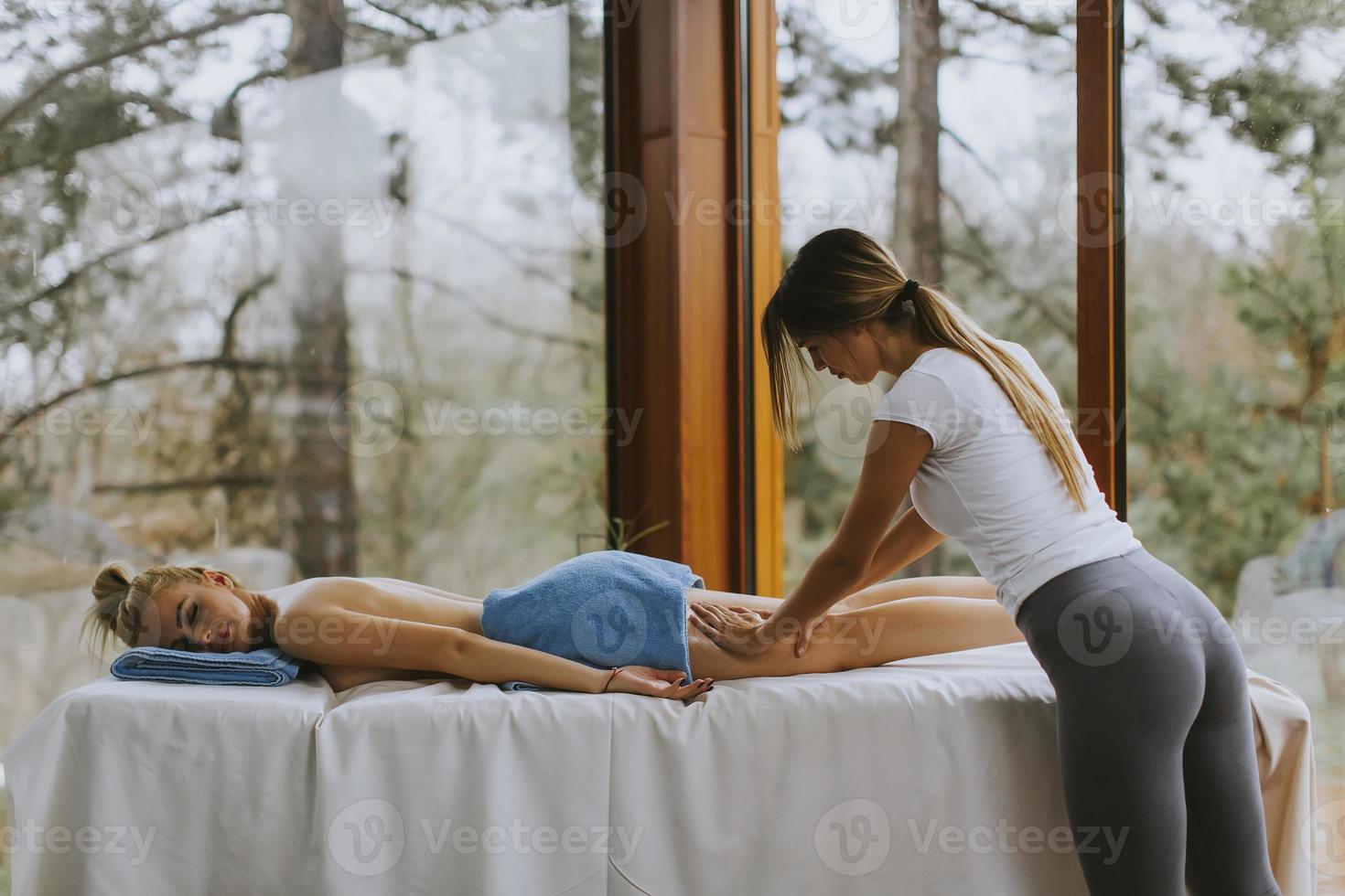 bella giovane donna sdraiata e con massaggio alle gambe nel salone spa durante la stagione invernale foto