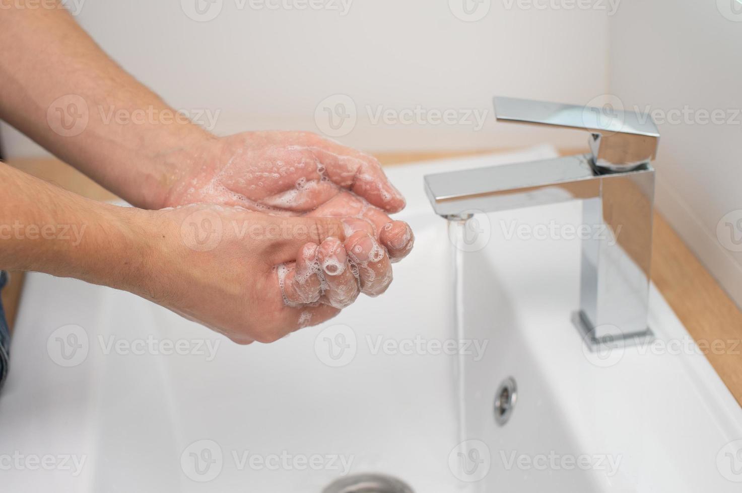Uomini mani con sapone e schiuma sotto un' ruscello di acqua nel il lavabo foto