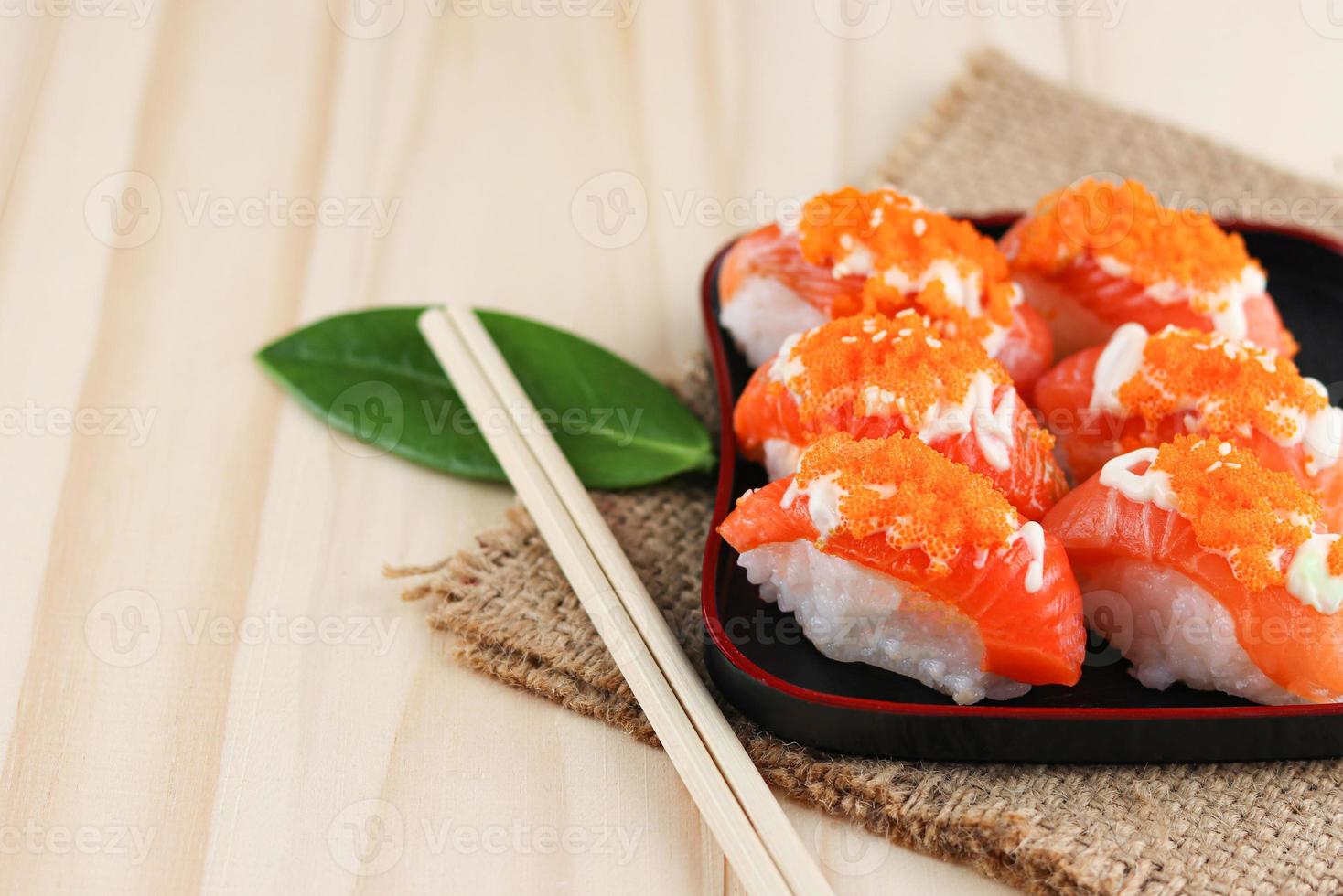 sushi di color salmone sulla banda nera e stuoia della tela da imballaggio con le bacchette sulla tavola di legno foto