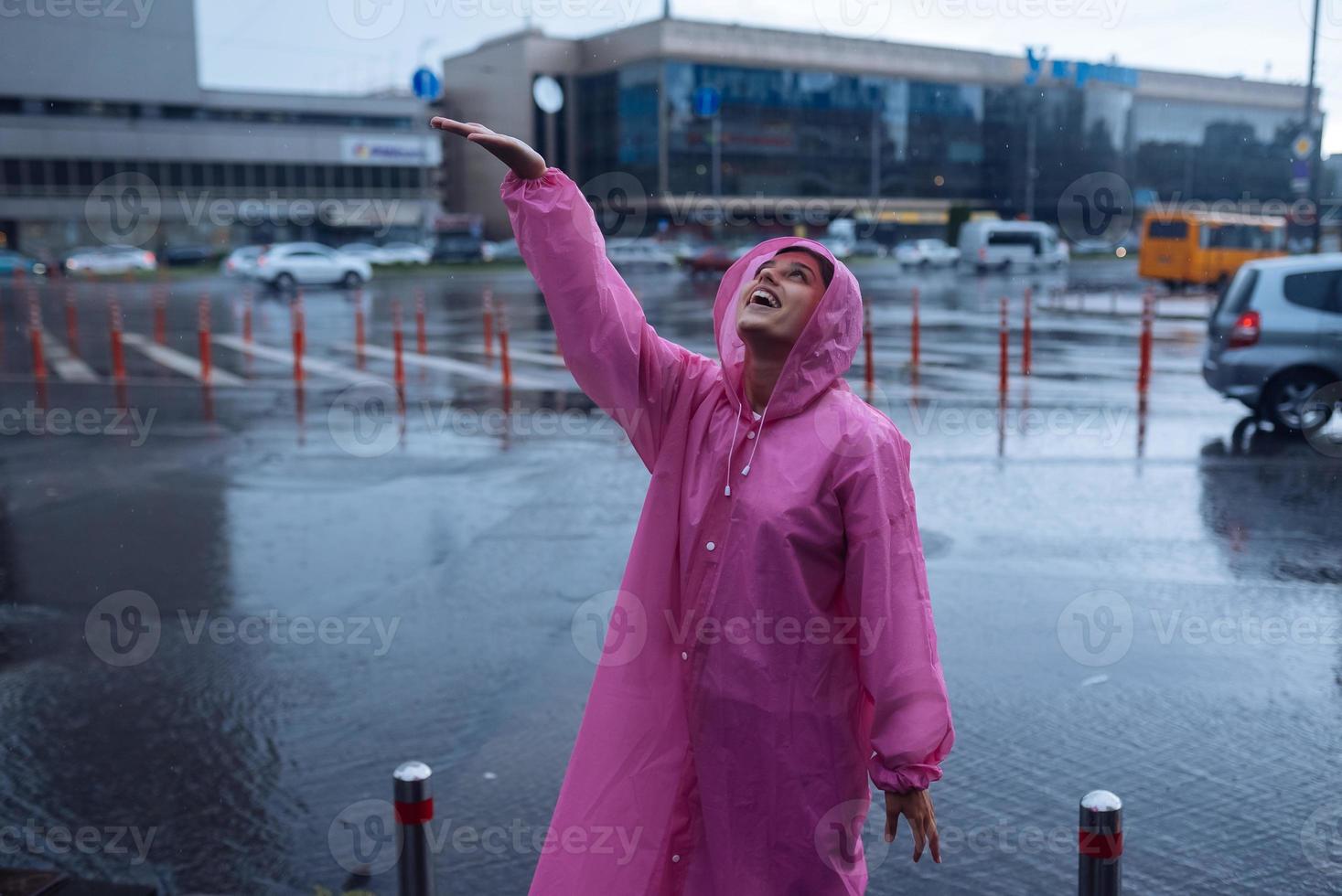 giovane sorridente donna nel un' rosa impermeabile godendo un' piovoso giorno. foto