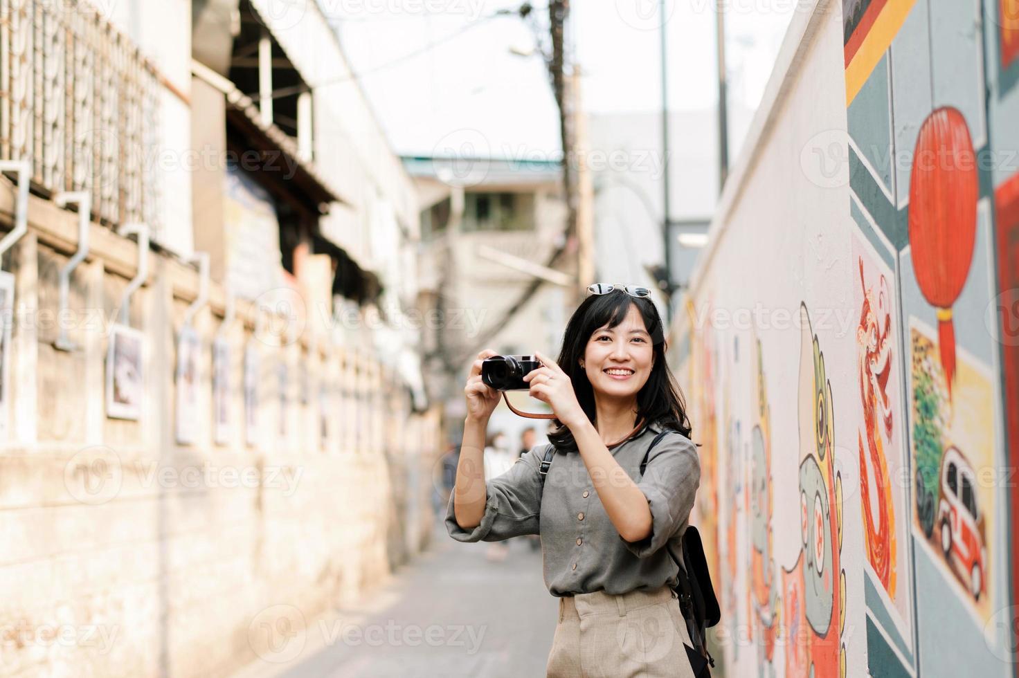 giovane asiatico donna zaino viaggiatore utilizzando digitale compatto telecamera, godendo strada culturale Locale posto e Sorridi. viaggiatore controllo su lato strade. foto