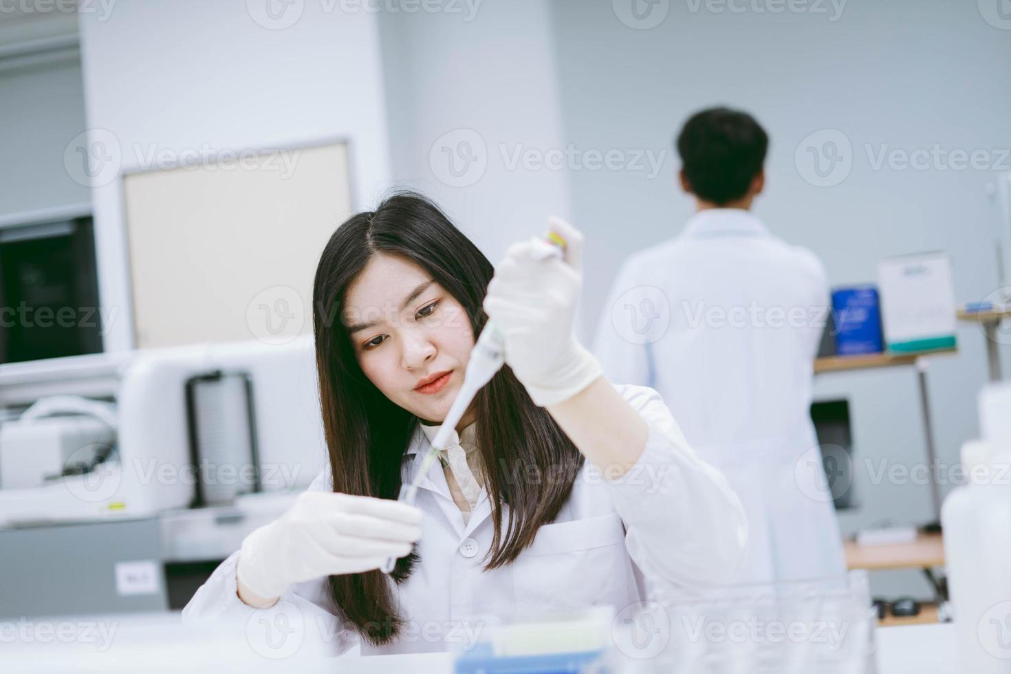 giovane scienziato medico che lavora in laboratorio medico, giovane scienziata che usa la pipetta automatica per trasferire il campione foto
