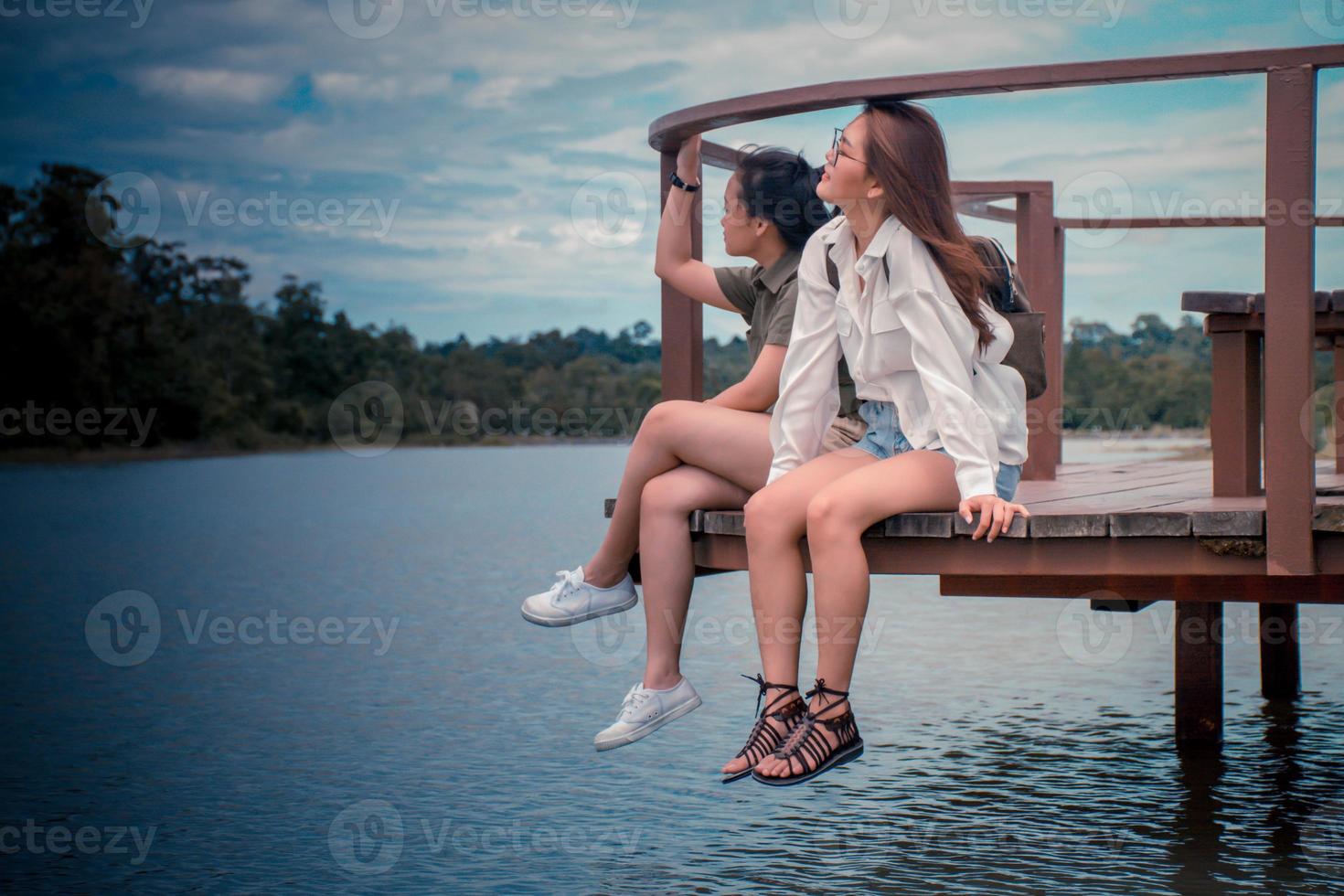 Due giovane Asia Da donna indossare bicchieri e zaino per viaggio il vacanze. Due ragazze era indossare un' bianca verde camicia seduta su il ponte e guardare a il bellissimo fiumi e montagne. rilassato. foto