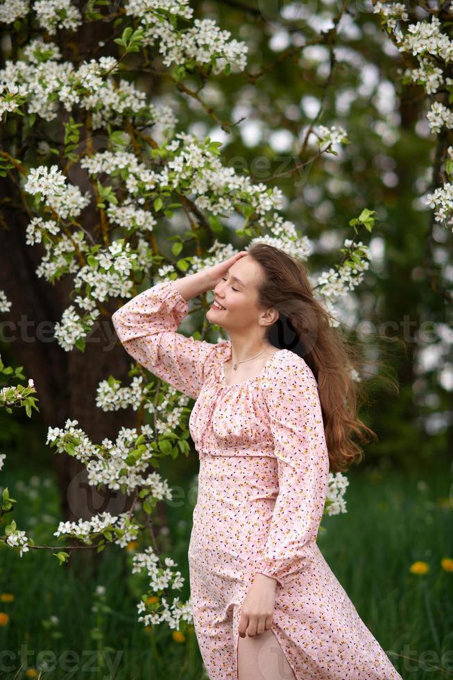 un' ragazza nel un' rosa vestito è in piedi sotto un' albero con sua occhi chiuso e sorridente foto