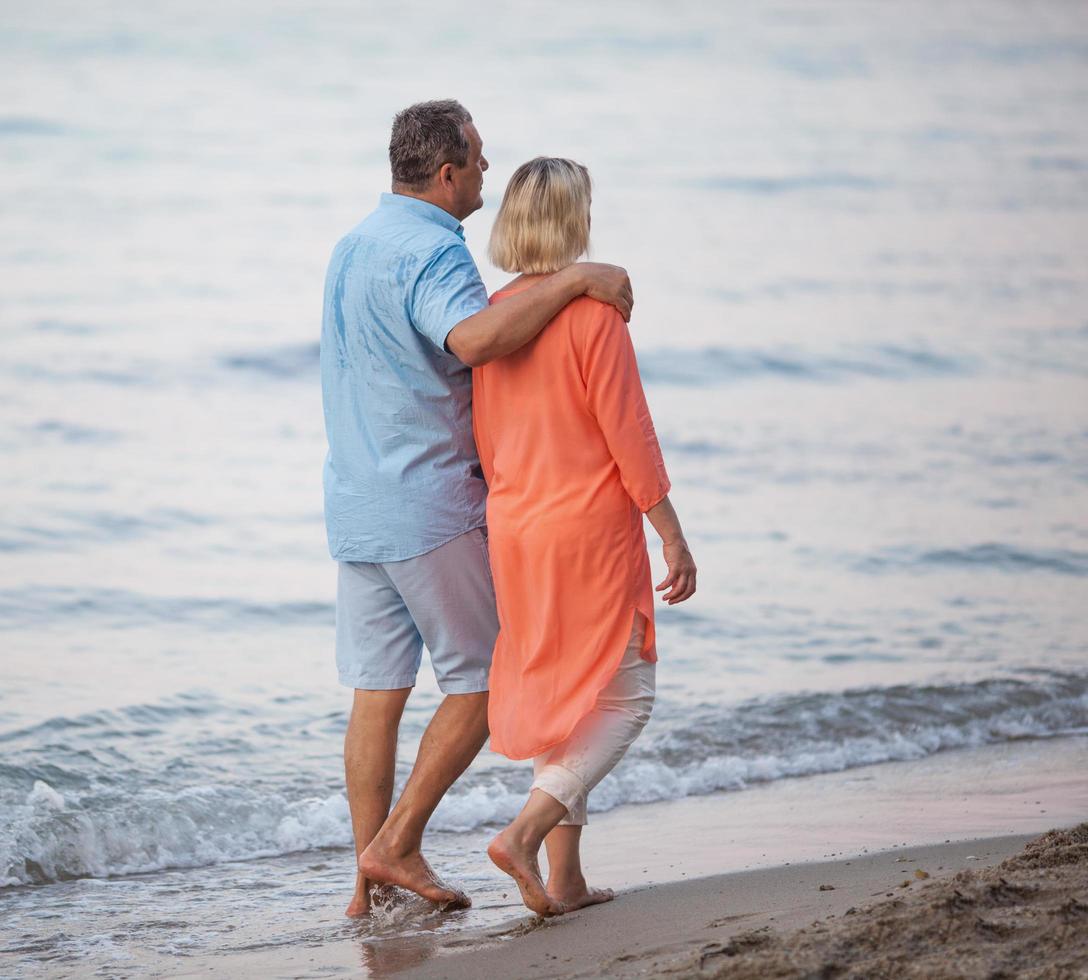 coppia matura godendo di una passeggiata a piedi nudi in spiaggia foto