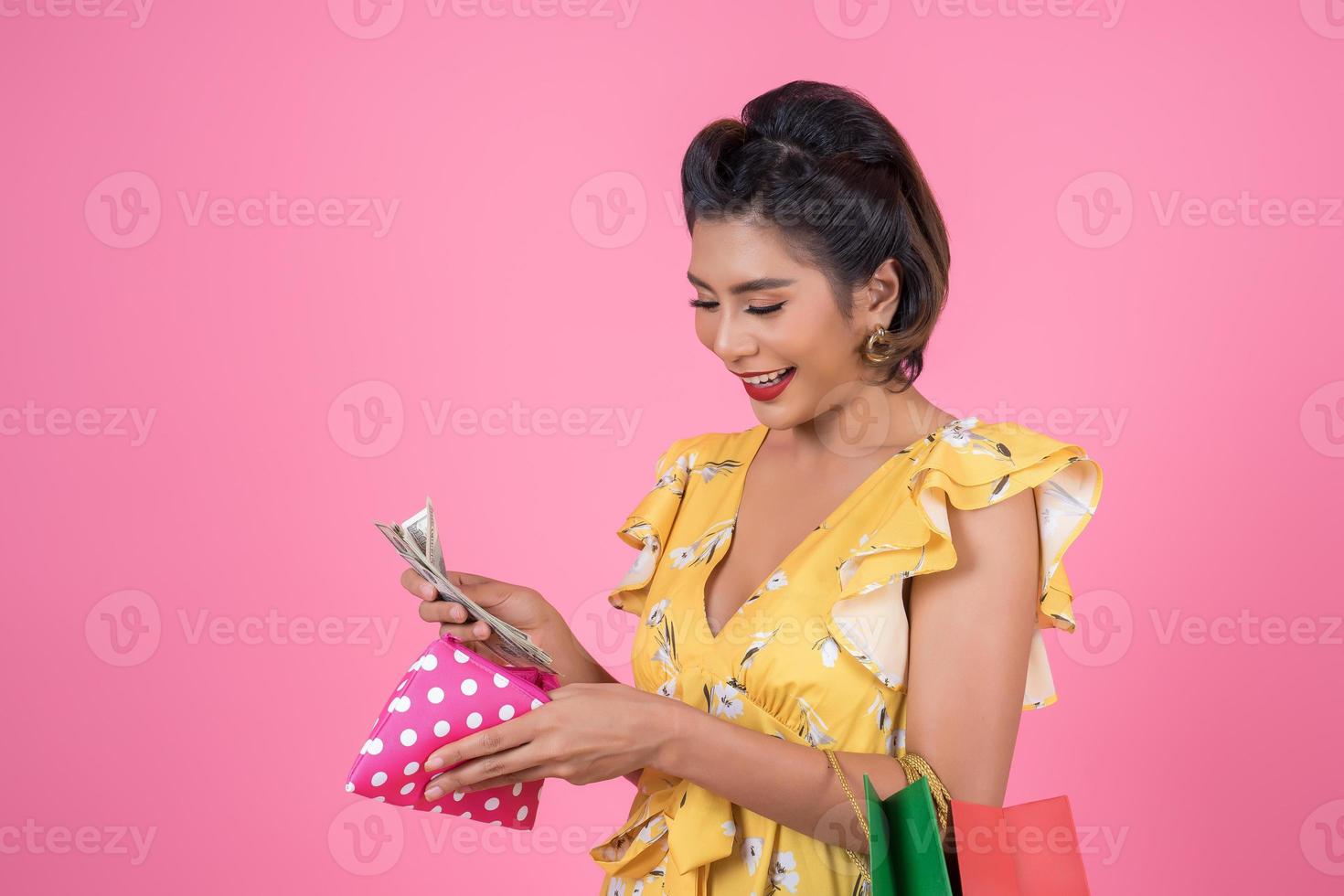 giovane donna alla moda che tiene un portafoglio con contanti e borse della spesa foto