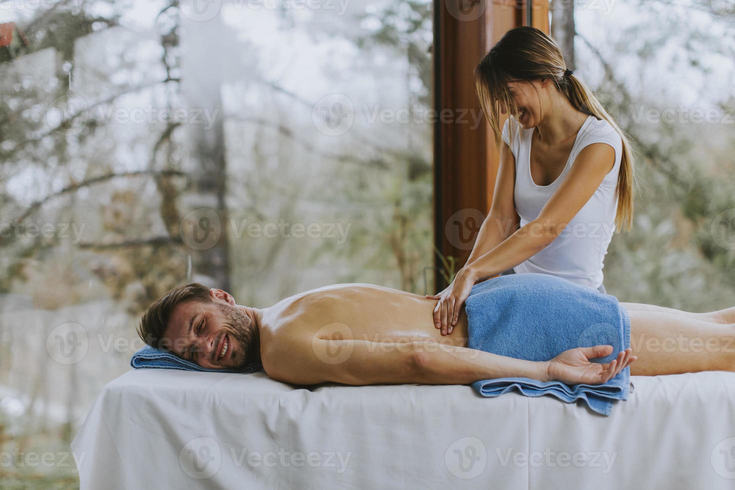 bel giovane uomo sdraiato e con massaggio alla schiena nel salone spa durante la stagione invernale foto