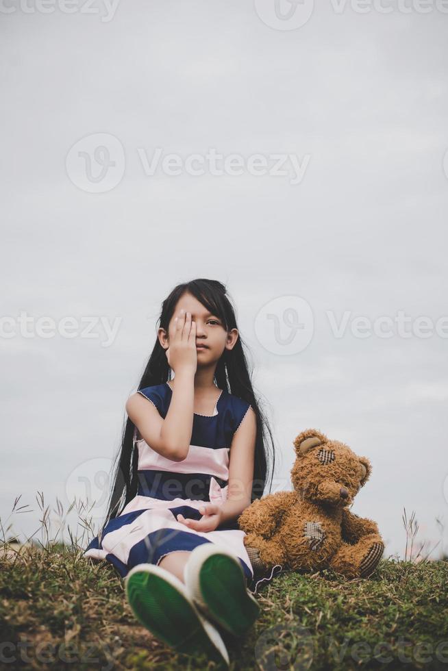 bambina seduta con il suo orso sconvolto in un campo di prato foto