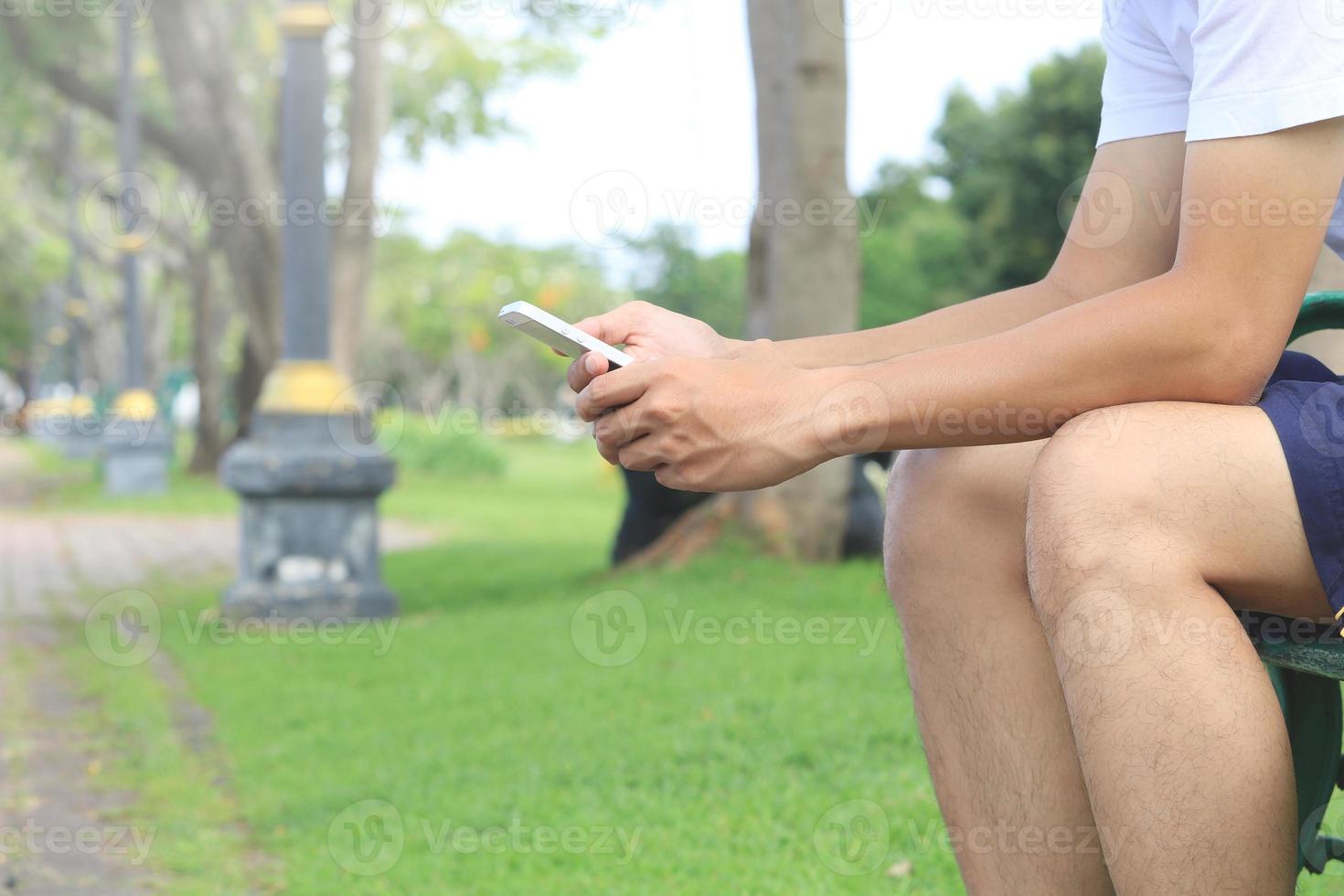 giovane uomo seduto su una panchina nel parco cellulare utilizzando il telefono nel parco pubblico foto