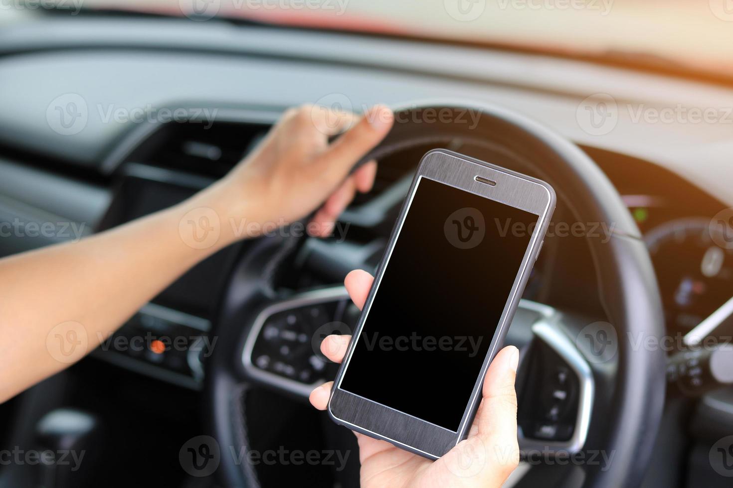 mani che tengono telefono cellulare e volante in interni auto foto
