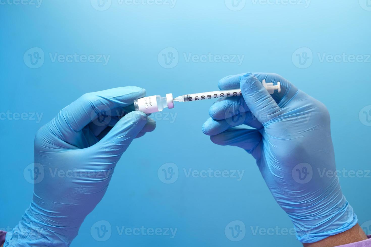 mano in guanti di lattice blu riempimento siringa con la medicina, isolato su sfondo blu foto
