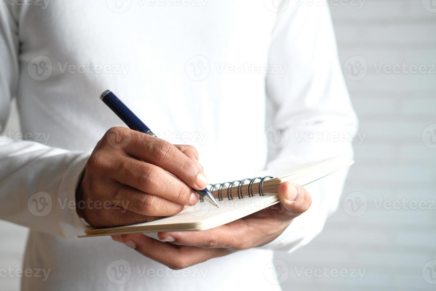 primo piano di un uomo in una camicia bianca casual scrivendo sul blocco note foto