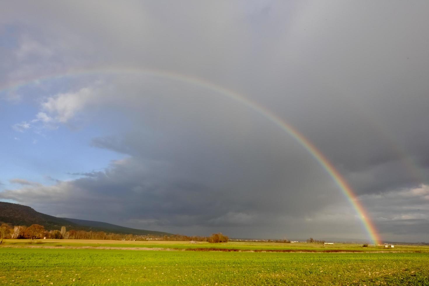 arcobaleno su buio pioggia nuvole al di sopra di verde i campi nel il inverno foto