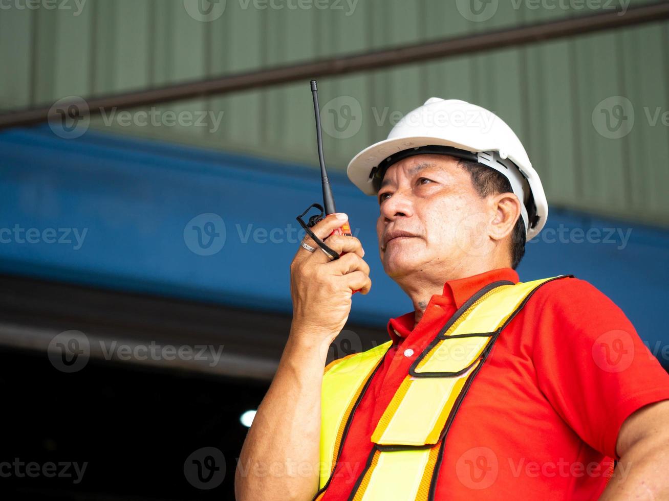 maschio persona supervisore direttore fabbrica azienda indossare bianca elmetto protettivo casco sicurezza talkie walkie Radio uomo In piedi controllo opera lavoro occupazione carriera controllo logistica importare esportare carico costruzione foto