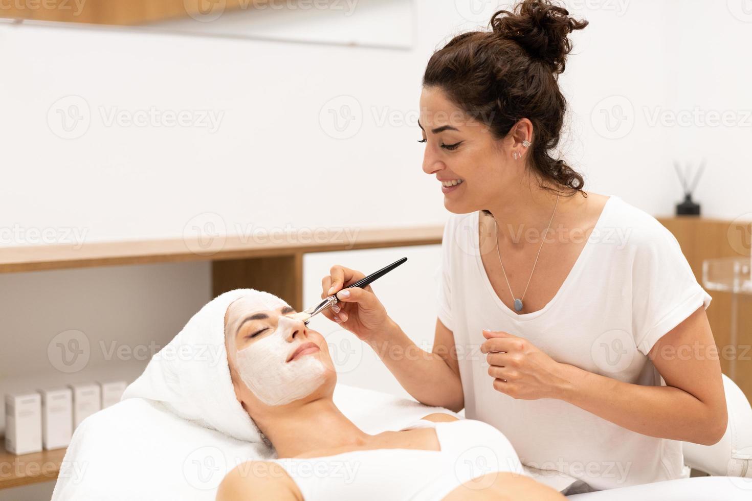 estetica applicando una maschera al viso di una donna di mezza età nel moderno centro benessere. foto