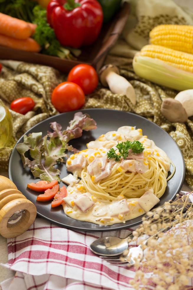 pasta alla carbonara con pancetta e parmigiano, lattuga e pomodori a fette su un piatto nero foto