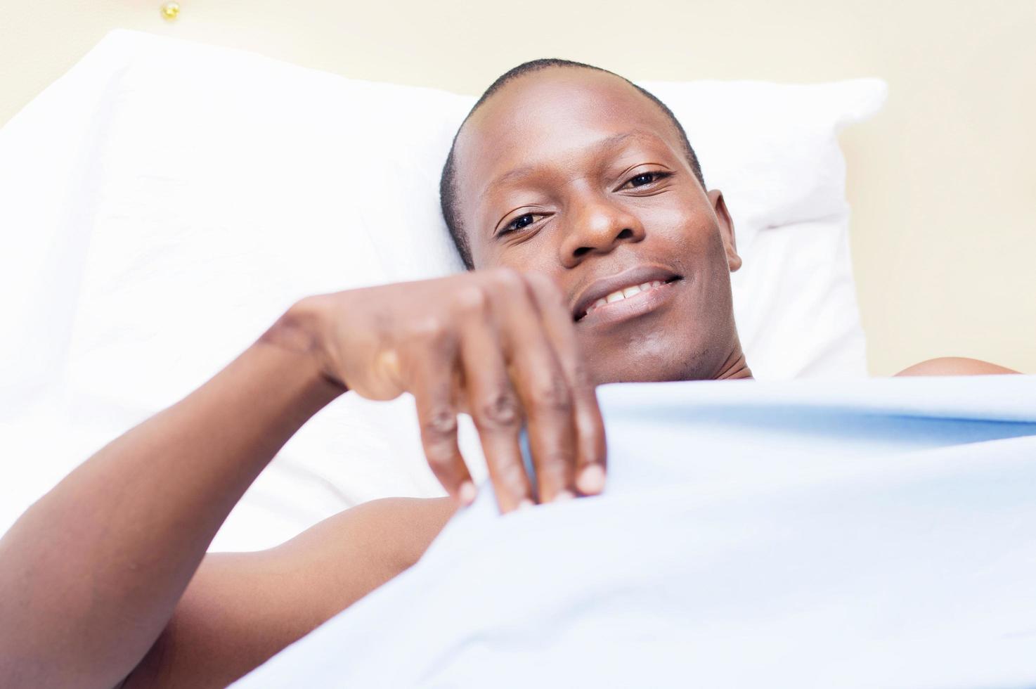uomo di colore sdraiato in un letto sorridente foto
