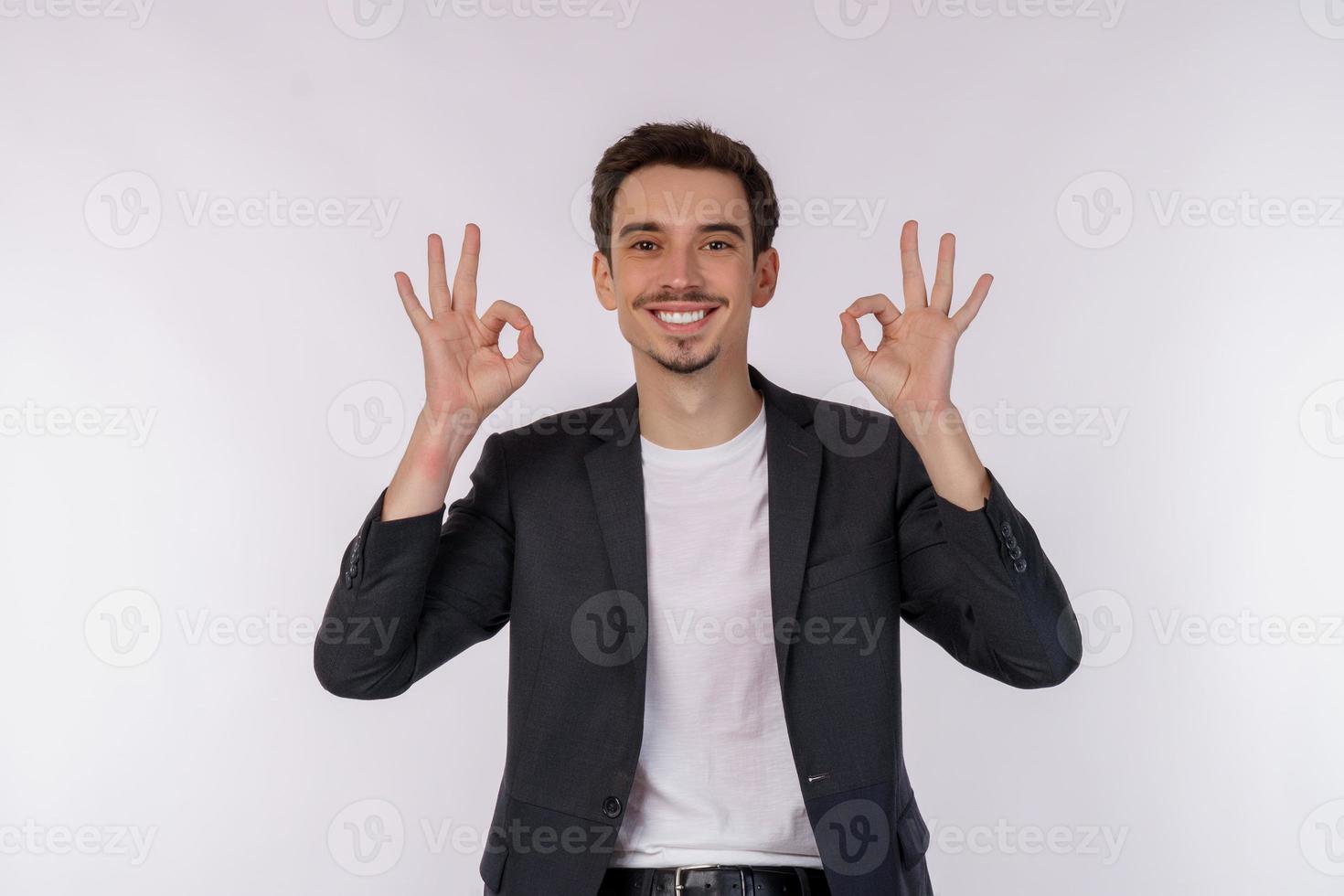 ritratto di contento giovane bello uomo d'affari fare ok cartello con mano e dita al di sopra di bianca sfondo foto