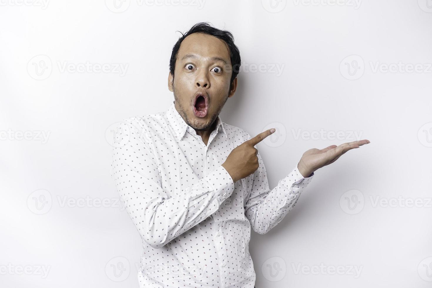 scioccato asiatico uomo indossare bianca camicia puntamento a il copia spazio accanto lui, isolato di bianca sfondo foto