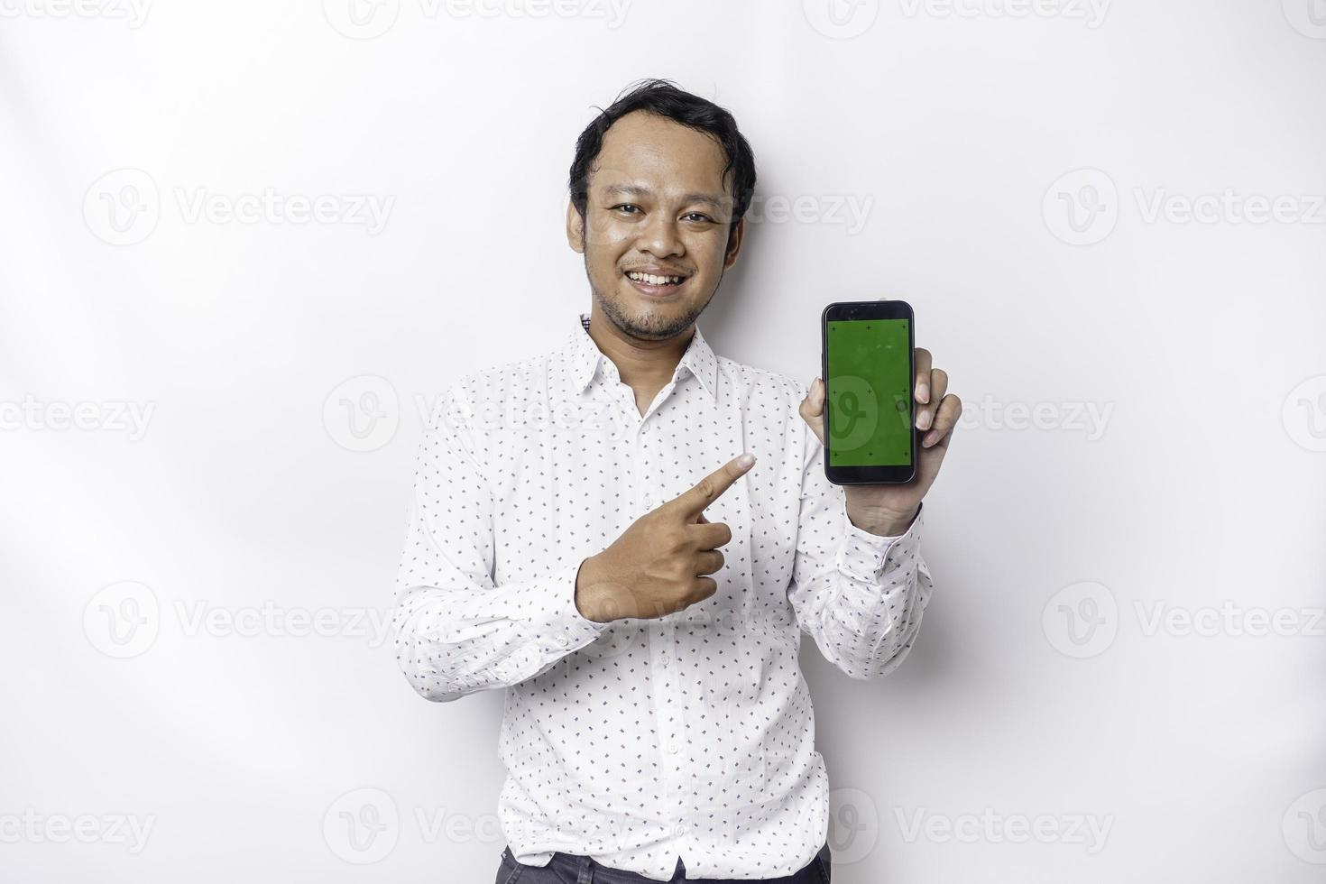 un' ritratto di un' sorridente asiatico uomo indossare un' bianca camicia e mostrando verde schermo su sua Telefono, isolato di bianca sfondo foto