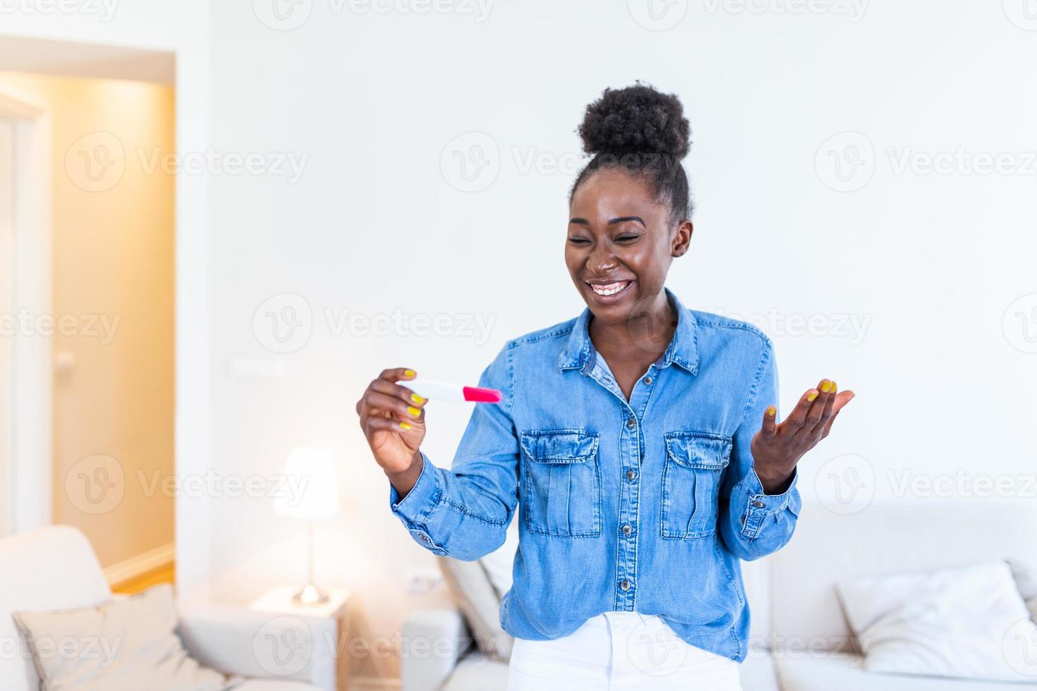 giovane donna guardare a gravidanza test nel felicità. infine incinta. attraente nero donne guardare a gravidanza test e sorridente mentre seduta su il divano a casa foto