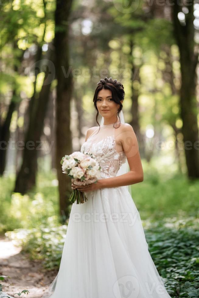ritratto di un elegante sposa ragazza su un' sentiero nel un' deciduo foresta con un' mazzo foto