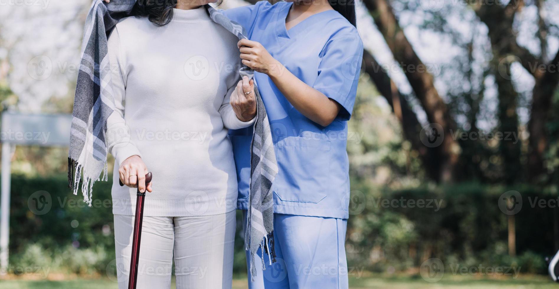 asiatico giovane badante infermiera supporto anziano più vecchio maschio a piedi all'aperto. specialista ragazza medico Aiuto e prendere cura di anziano maturo uomo paziente fare fisico terapia nel pubblico parco a assistenza infermieristica casa. foto