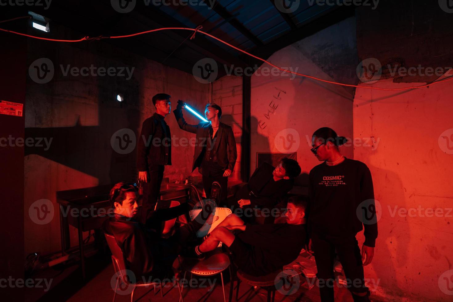 un' gruppo di asiatico adolescenti nel nero Abiti in posa molto cattivo con loro amici nel un' magazzino con un' rosso leggero foto
