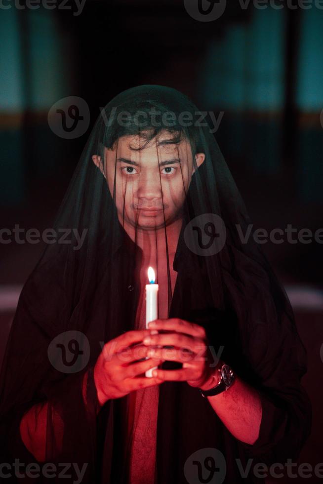 un asiatico uomo con un' trasparente cappuccio coperto nel sangue detiene un' candela nel il suo mano con un' molto pauroso espressione foto