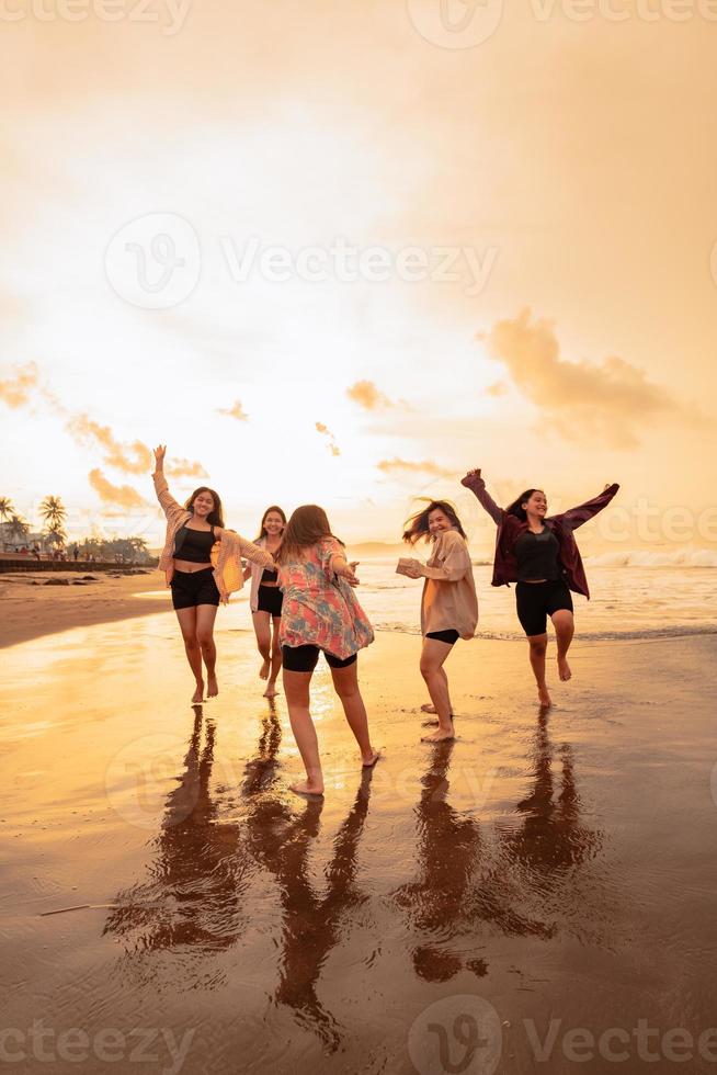 un' gruppo di asiatico adolescenti nel camicie in esecuzione con loro amici con molto allegro espressioni su il spiaggia foto