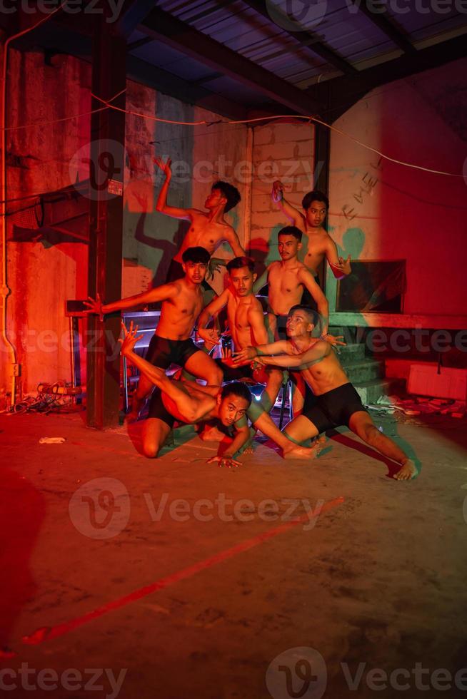 un' gruppo di uomini senza Abiti danza pose nel un vecchio edificio con un' rosso leggero foto