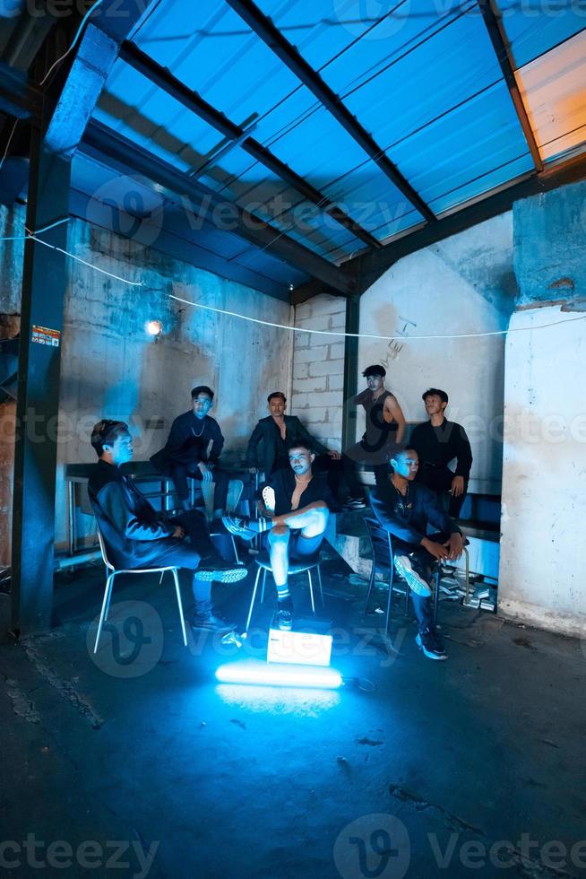 un' gruppo di asiatico adolescenti nel nero Abiti seduta insieme nel un' nero edificio con un' blu leggero su il camera foto