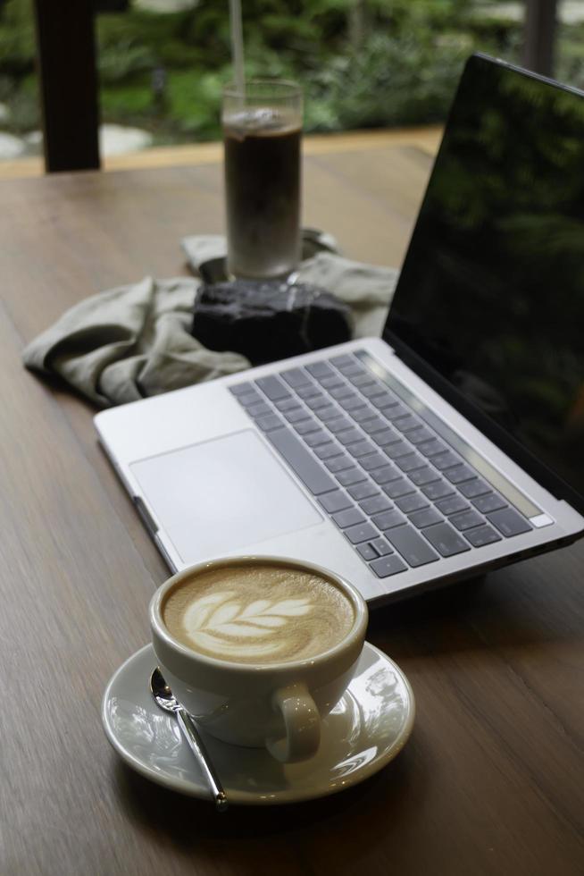 caffè latte caldo su un tavolo di legno con un computer portatile foto