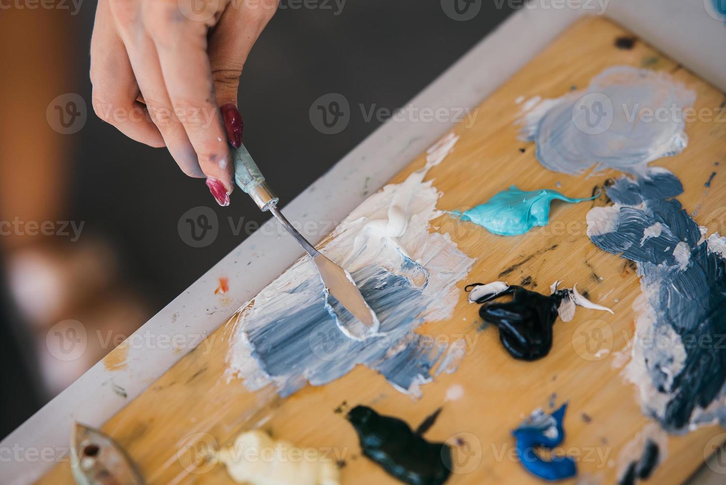 vicino su di donna di mano mescolare vernici nel tavolozza foto