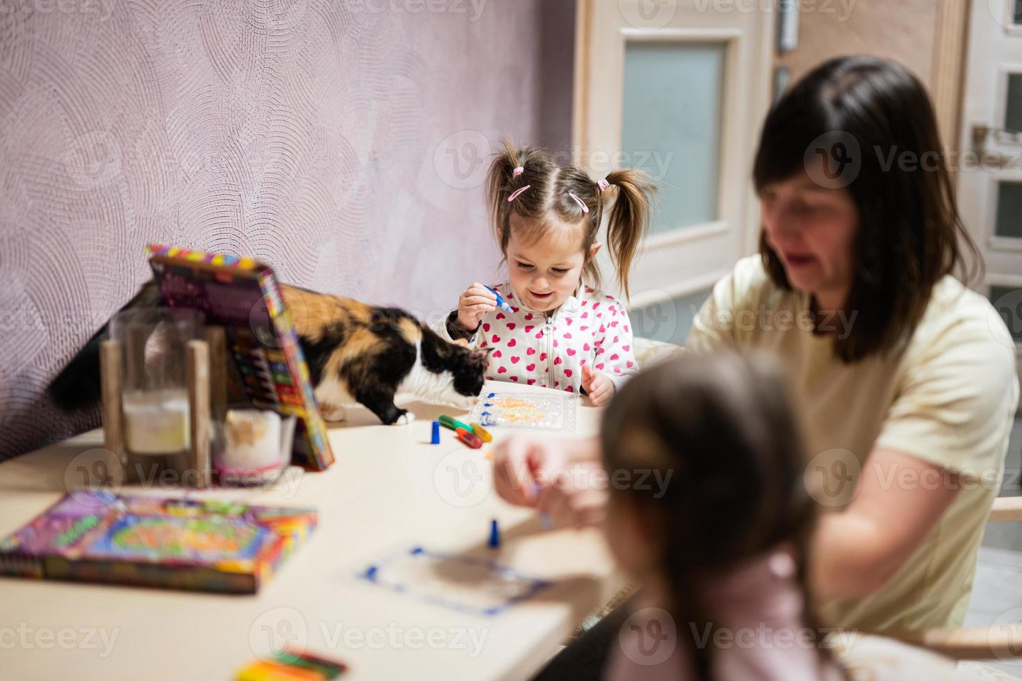 madre e figlie decorazione arte con luccichio arredamento. anche gatto con loro su tavolo. foto