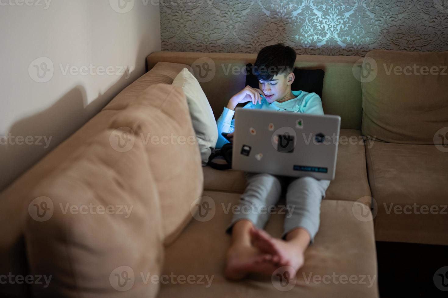 giovane adolescente ragazzo nel davanti di un' il computer portatile su un' letto a sera. foto